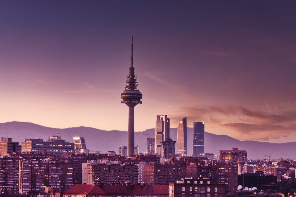 City skyline at sunset featuring modern skyscrapers and a prominent communication tower.