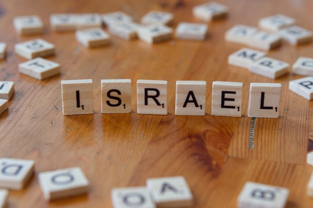 Wooden letter tiles spelling "ISRAEL" on a wooden table surface with scattered tiles around.