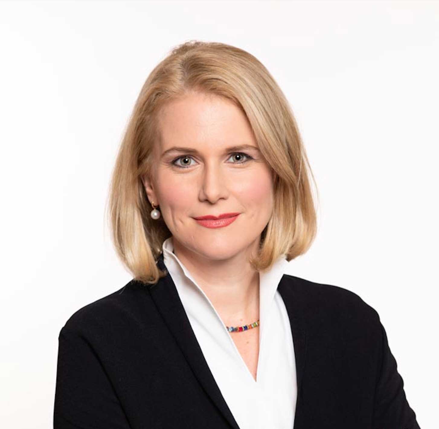 Attorney with blonde hair wearing a dark blazer and white blouse, looking confidently at the camera against a light background.