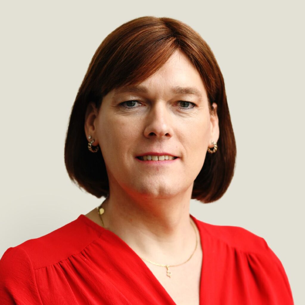 Professional woman with shoulder-length brown hair wearing a red blouse, posed against a neutral background.