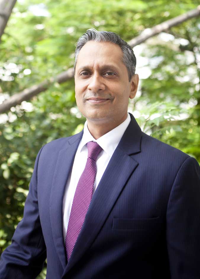 Legal professional posed outdoors in a suit with greenery in the background, looking confidently at the camera.