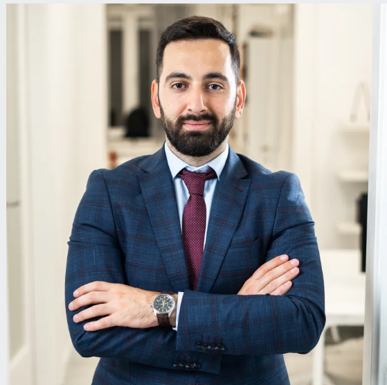 Lawyer posing with arms crossed in a modern office setting, dressed in a suit and tie.