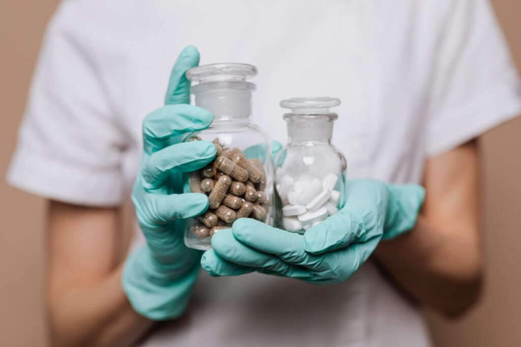 Healthcare professional holding two glass containers with capsules and tablets.