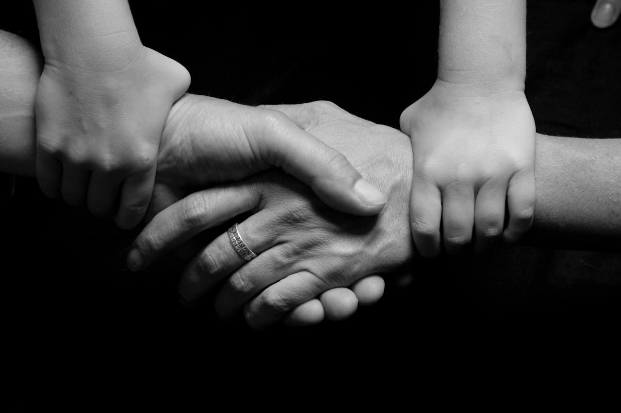 Hands of adults and a child clasped together, symbolizing unity and support in a familial context.