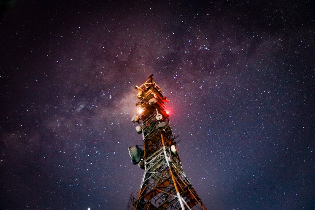 Communication tower illuminated against a night sky filled with stars and the Milky Way.