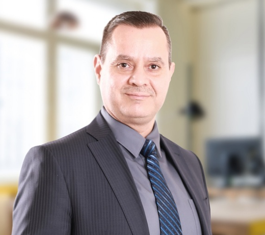 Attorney in a suit standing confidently in a law office with modern decor and visible office equipment in background.