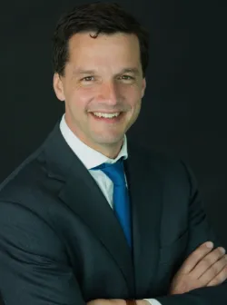 Lawyer smiling with arms crossed, wearing a suit and tie, against a dark background.