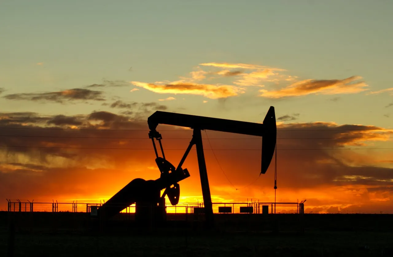 Oil pump jack silhouetted against a vibrant sunset sky in an industrial setting.