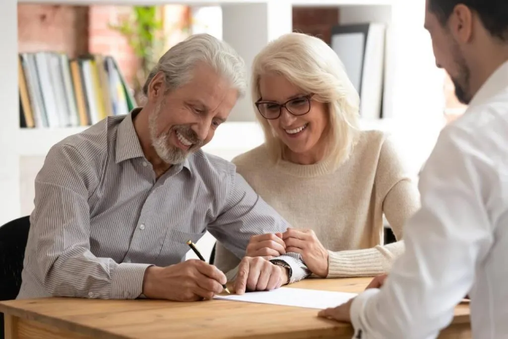 Older couple happily reviewing and signing legal documents with an attorney in a law office setting.