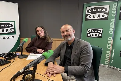 Radio hosts seated at a desk with microphones, discussing on-air at Onda Cero studio.