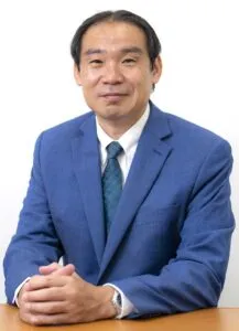 Lawyer in a blue suit sitting at a table, with hands clasped, in a professional legal setting.