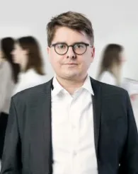 Lawyer in professional attire, standing confidently with blurred figures of colleagues in the background.