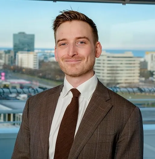 Lawyer smiling in a professional suit with a city skyline visible in the background.