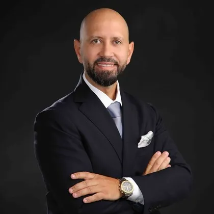 Lawyer in a suit, arms crossed, standing against a neutral background, conveying professionalism and confidence.