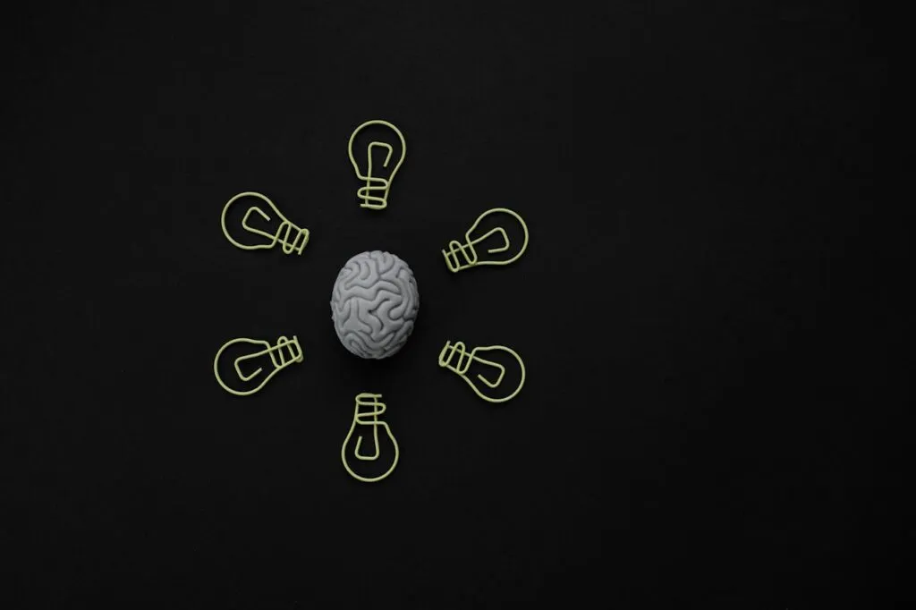 Brain model surrounded by lightbulb paper clips on a black background, representing creativity and ideas.