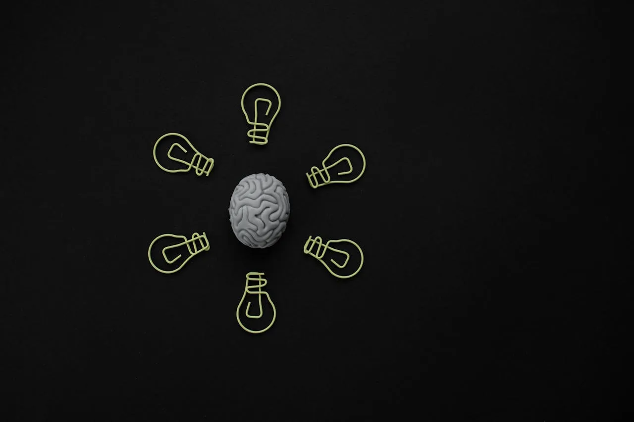 Brain model surrounded by lightbulb paper clips on a black background, representing creativity and ideas.