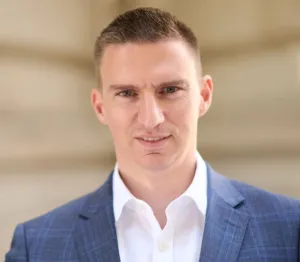 Professional man in a suit smiling, standing outside in a legal environment.