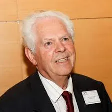 Elderly man in suit smiling at camera, likely attending a legal conference or networking event.