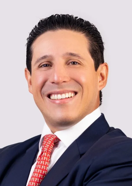 Smiling attorney in suit with a red tie, posing confidently against a neutral background.