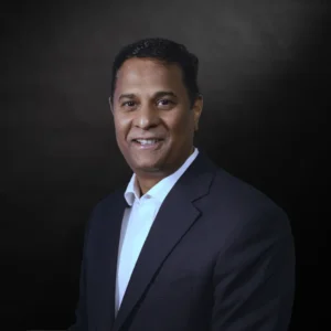 Professional man in a suit smiling, standing against a neutral background.