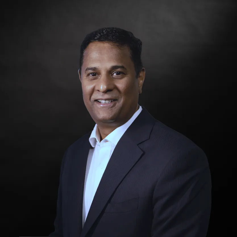 Professional man in a suit smiling, standing against a neutral background.