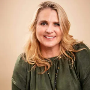 Experienced legal professional smiling, wearing a green blouse, with blonde hair, against a neutral background.