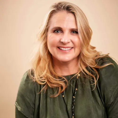 Experienced legal professional smiling, wearing a green blouse, with blonde hair, against a neutral background.