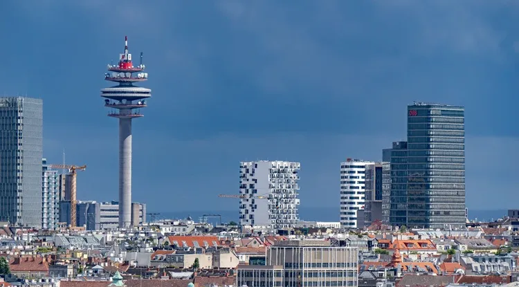City skyline featuring a communication tower and modern office buildings under a cloudy sky.