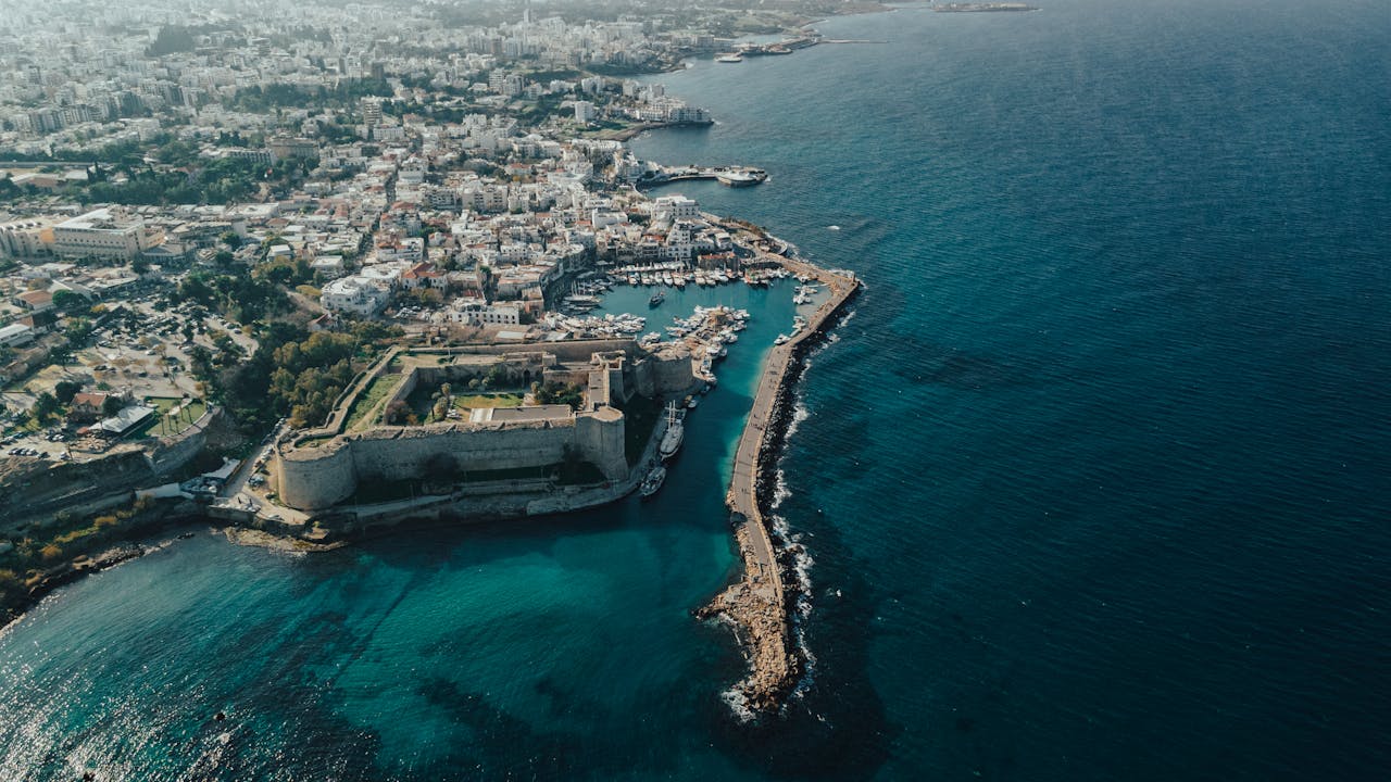 Aerial view of a coastal city featuring a historic fortress and marina along the clear blue water.