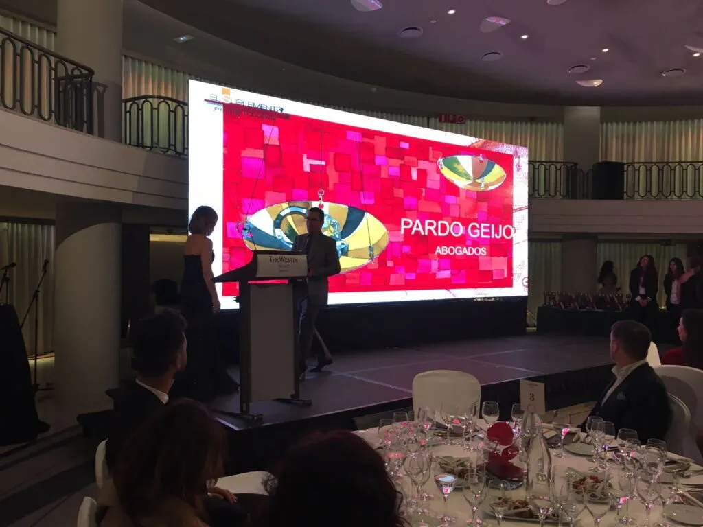 Attorney presenting at an awards ceremony with large banner displaying law firm name and decorated tables.