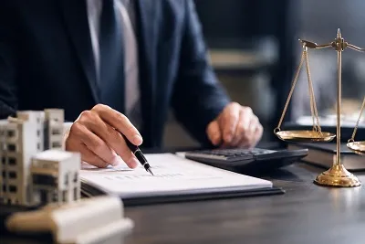 Lawyer reviewing documents with pen at desk, with scales of justice in background.