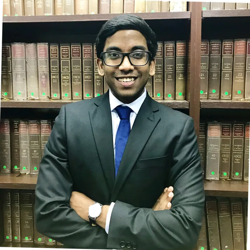 Lawyer standing confidently with arms crossed in front of a bookshelf filled with law books.