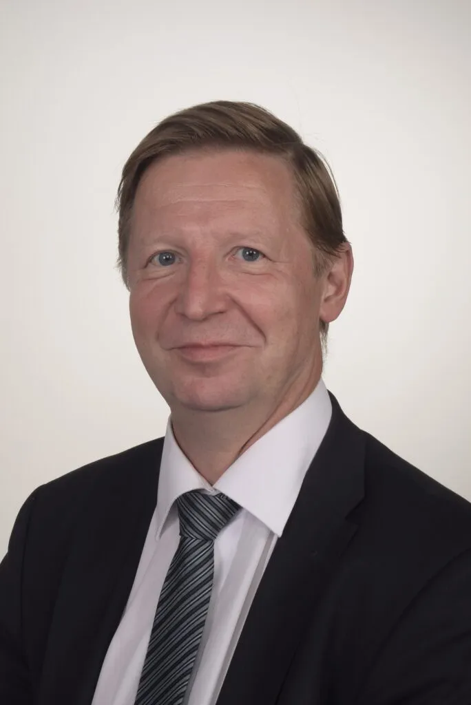 Lawyer with short hair, wearing a suit and tie, smiling against a neutral background.