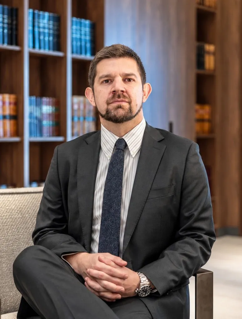 Lawyer seated in an office with law books in the background, displaying a professional demeanor.