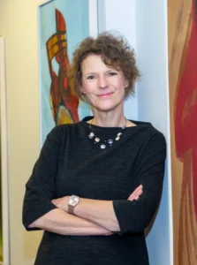 Legal professional standing confidently with arms crossed in an office setting, featuring abstract artwork in the background.