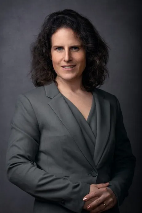 Female attorney in a professional gray suit, smiling with arms crossed, against a dark background.