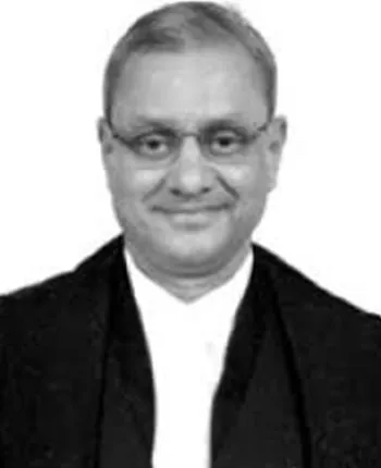 Judge in formal attire with glasses, presenting a professional demeanor in a neutral setting.