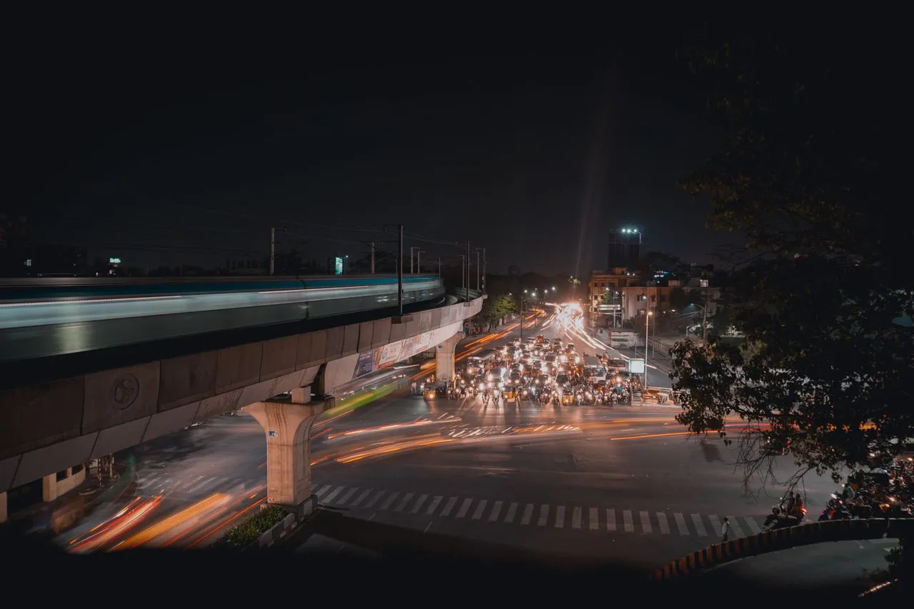 Nighttime urban scene with traffic lights illuminating busy intersection and an elevated train track above.