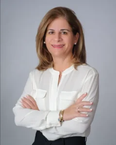 Lawyer posing with arms crossed, wearing a white blouse and smiling against a neutral background.