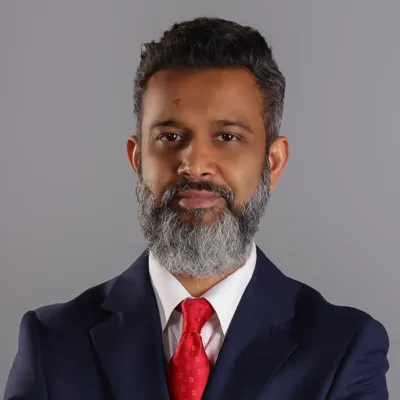 Professional man with gray beard, wearing a suit and red tie, poses with arms crossed against a neutral background.