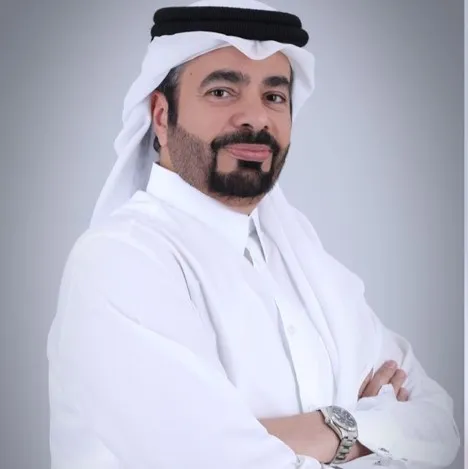 Lawyer posing confidently with arms crossed, dressed in traditional attire against a neutral background.